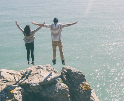 A couple on top of cliff looking over the ocean.